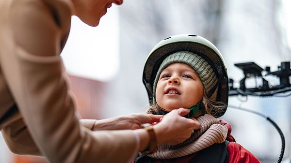 Kind bekommt Fahrradhelm über die Mütze geschnallt (Themenbild) - Foto: miniseries/iStock