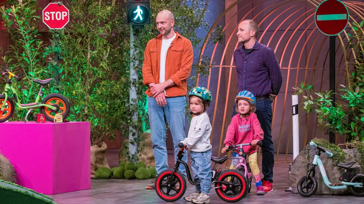Zwei Mädchen mit Laufrädern stehen in einem Fernsehstudio. Hinter ihnen stehen zwei Männer