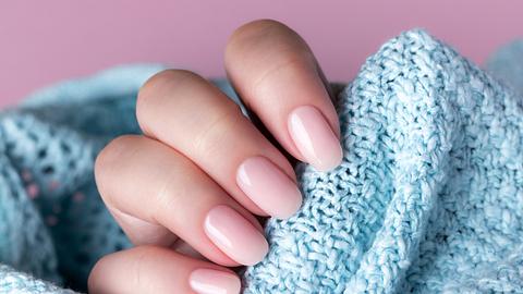 Frauenhand in blauen Pullover mit hellrosa Nägeln - Foto: iStock/ Mariia Demchenko