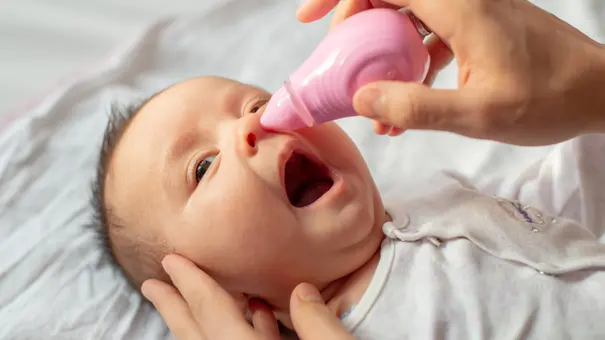 Mutter macht ihrem baby mit einem rosa Nasensauger die Nase sauber. - Foto: iStock/Tutye