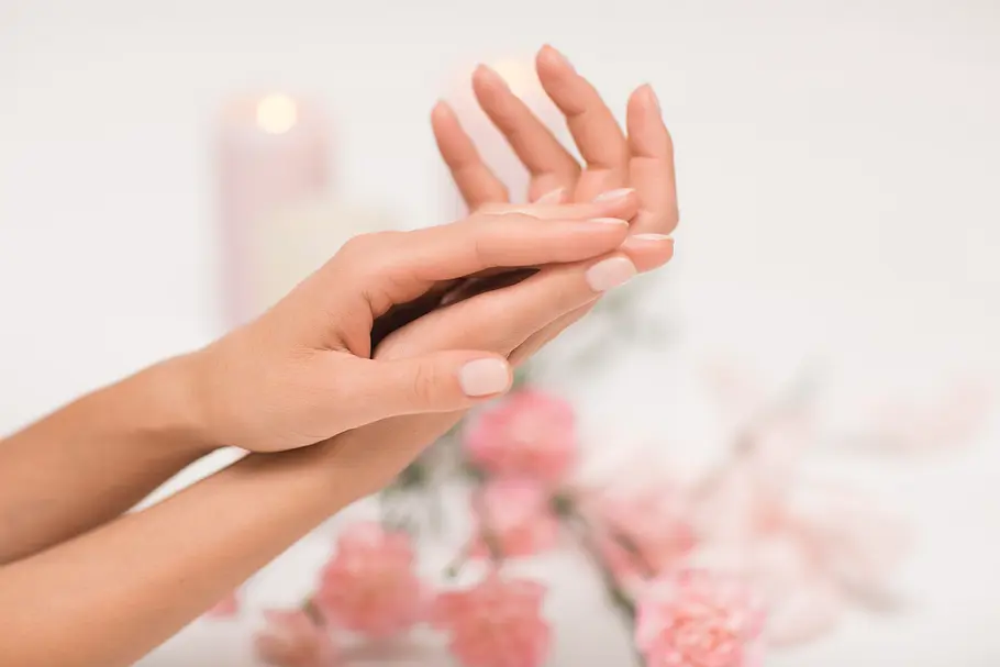 Natürliche Fingernägel Hände mit kurzen, dezent lackierten Nägeln, im Hintergrund liegen Blumen