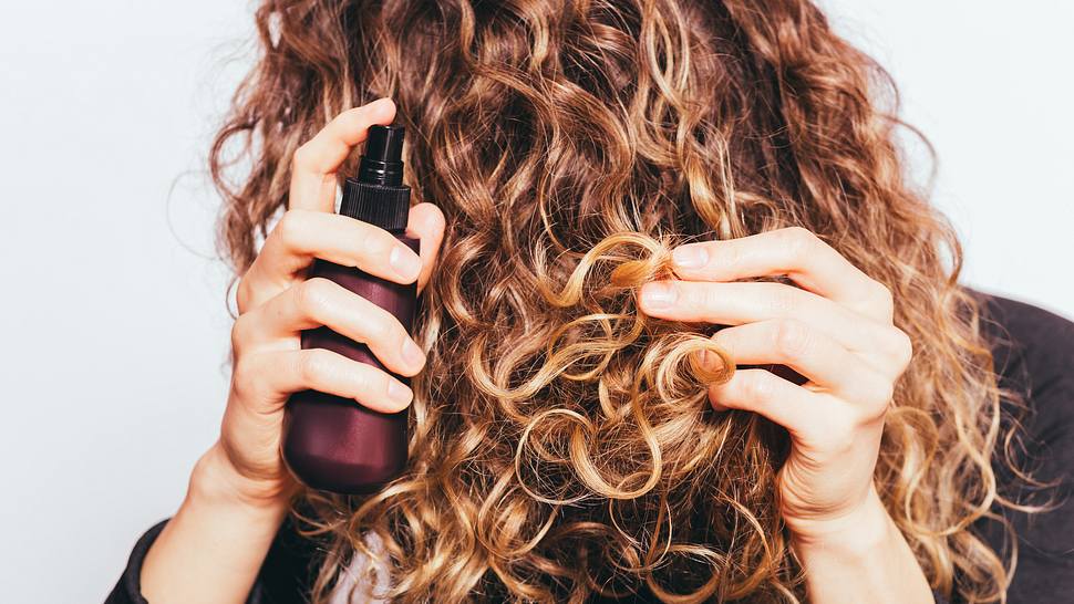 Frau die sich Haar-Pflege in die Locken sprüht  - Foto: iprogressman/iStock (Themenbild)