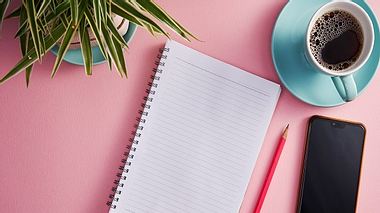 Notizbuch, Stift, Handy, Kaffeetasse und Topfblume vor rosa Hintergrund - Foto: iStock/new look casting