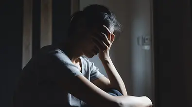 Frau sitzt auf dem Boden. Ihr geht es nicht gut, sie verbirgt ihre Augen in der Hand. - Foto: Tinnakorn Jorruang / iStock