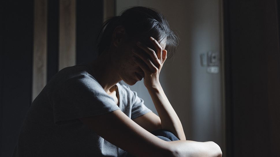 Frau sitzt auf dem Boden. Ihr geht es nicht gut, sie verbirgt ihre Augen in der Hand. - Foto: Tinnakorn Jorruang / iStock