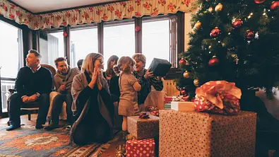 Eine Familie sitzt an Weihnachten zusammen und packt Geschenke aus. - Foto: istock/LeoPatrizi