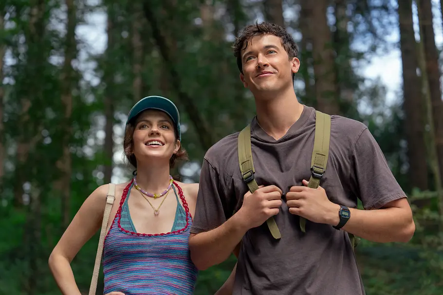 Zwei junge Menschen wandern fröhlich durch einen grünen Wald und blicken lächelnd in die Ferne.