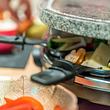 Raclette Grill mit Pfännchen und Zutaten auf dem Esstisch. - Foto: yevtony/iStock