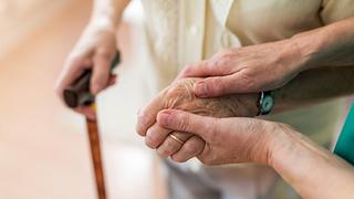 Nahaufnahme von Händen einer jüngeren Person, die die Hand einer älteren Person am Krückstock hält. - Foto: PIKSEL/iStock