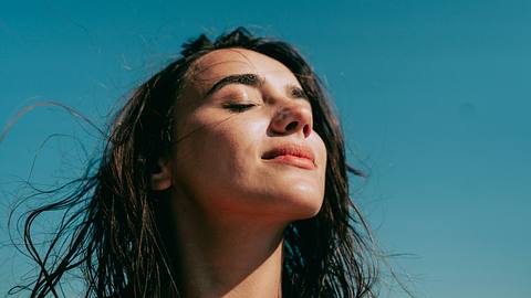 Frau sonnt ihr Gesicht vor blauem Himmel (Themenbild) - Foto: AleksandarNakic/iStock