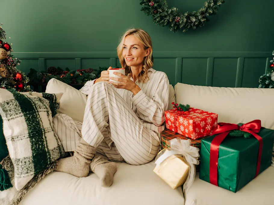 Pyjama für Weihnachten Blonde Frau im Pyjama sitzt mit Teetasse auf der Couch neben dem Weihnachtsbaum
