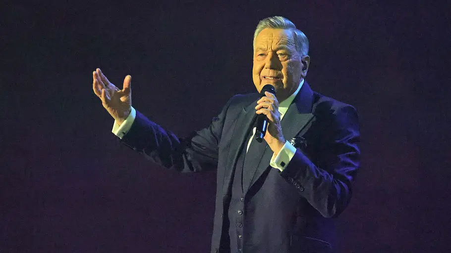 Roland Kaiser Roland Kaiser steht im Anzug auf der Bühne. Er hält sich ein Mikrofon an den Mund und streckt den anderen Arm zur Seite aus.