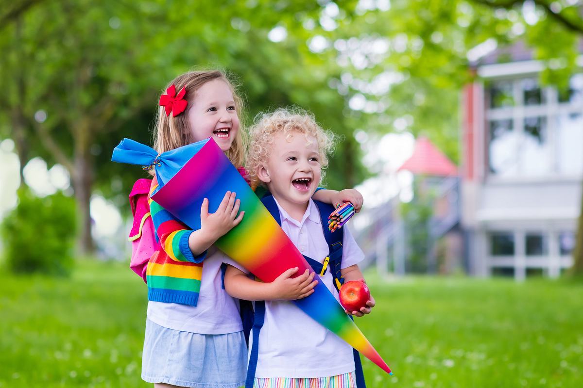 Kinder mit Regenbogenschultüte, Apfel und Stiften (Themenbild)