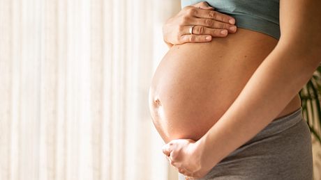 Frau streicht über ihren Babybauch - Foto: iStock/ SanyaSM