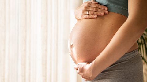 Frau streicht über ihren Babybauch - Foto: iStock/ SanyaSM