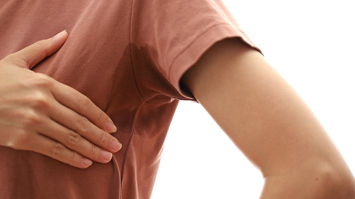 Frau fasst mit Hand an Schweißfleck unter der Achsel (Themenbild) - Foto: Pikusisi-Studio/iStock