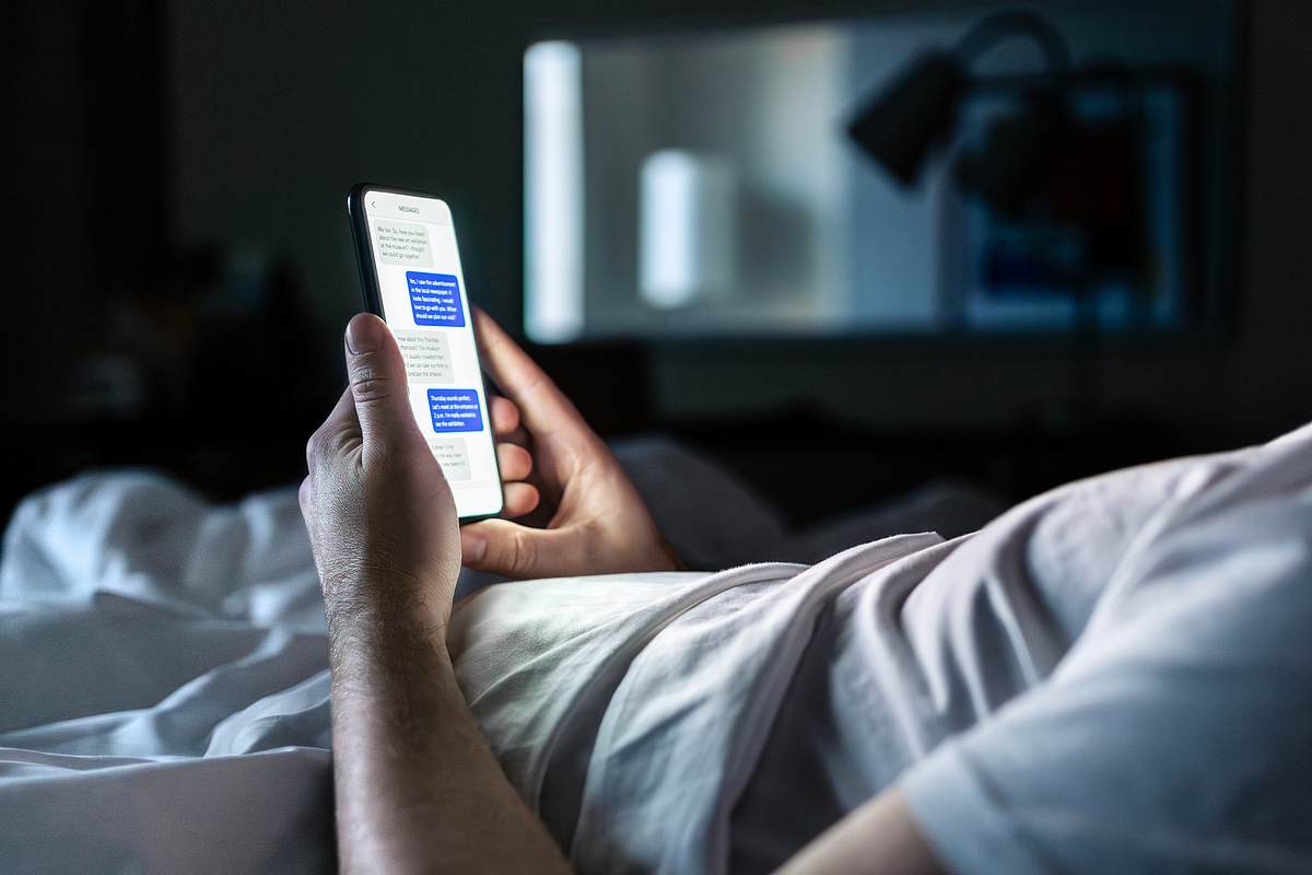 Mann liegt im Bett und liest Nachrichten auf seinem Handy.