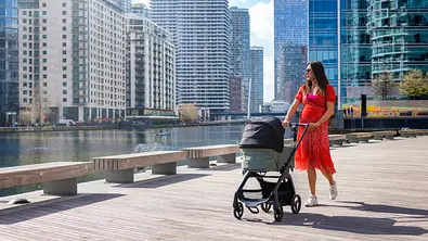 Frau schiebt einen Kinderwagen vor luxuriösen Hochhäusern. - Foto: iStock / SHansche