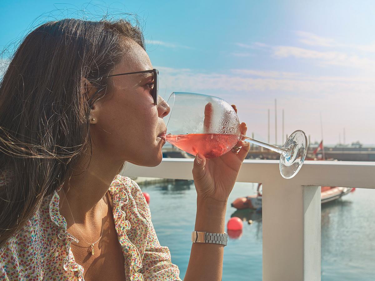 Junge Frau trinkt einen pinken Cocktail am Wasser
