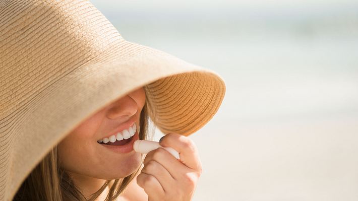 frau mit sonnenhut trägt pflegelippenstift auf - Foto: Getty / Tetra Images - Jamie Grill