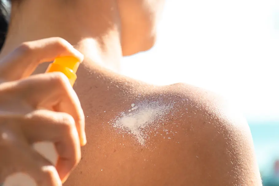 Hand einer Frau, die Sonnencreme auf die Schulter ihrer Freundin aufträgt.