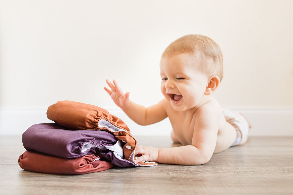 Baby liegend vor einem Stapel bunter Stoffwindeln 