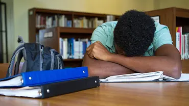 Ein Junge liegt mit dem Kopf auf seinem Schulbuch. - Foto: iStock / pixelheadphoto