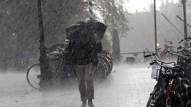 Eine Frau läuft mit einem Regenschirm durch einen Sturm mit Regen in der Stadt. - Foto: Doctor_bass/iStock