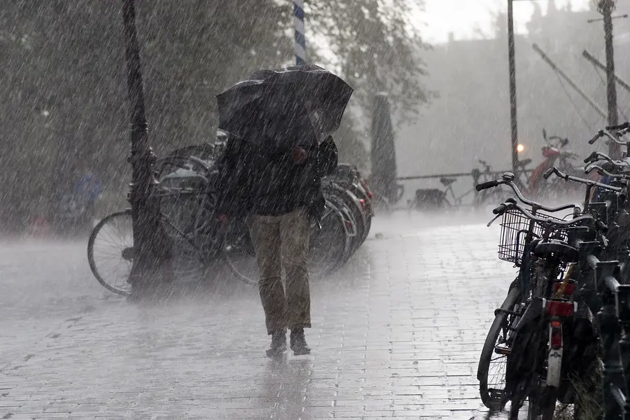 Sturm und Regen: HIER wird es diese Woche ungemütlich Eine Frau läuft mit einem Regenschirm durch einen Sturm mit Regen in der Stadt.