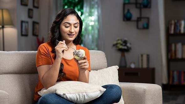 Frau isst Eis auf der Couch - Foto: Deepak Sethi/iStock
