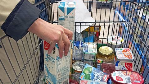 Nahaufnahme: Hand einer Frau, die Milch in einen vollen Einkaufswagen stellt. - Foto: IMAGO / Martin Wagner