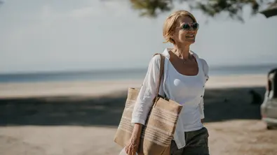 Frau in weißer Bluse geht am Strand.  - Foto: iStock/freemixer