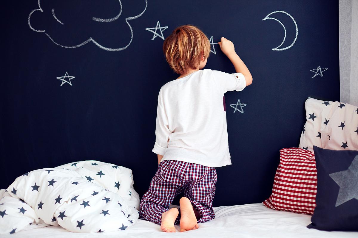 Kind malt mit Kreide auf einer Wand mit Tafelfarbe