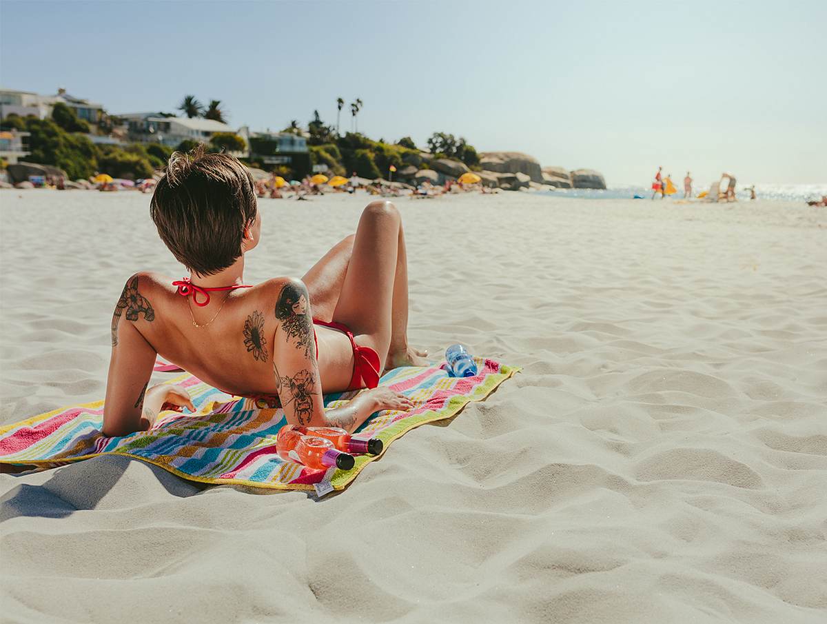 Frau mit Tattoos sonnt sich am Strand.