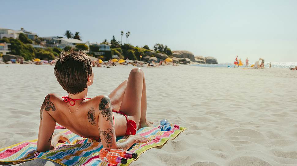 Frau mit Tattoos sonnt sich am Strand. - Foto: iStock/ jacoblund