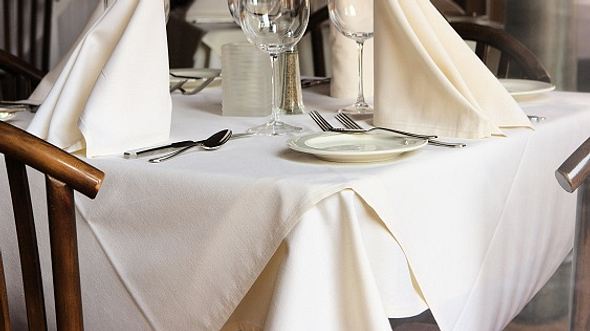 Gedeckter Tisch mit weißer Tischdecke und cremefarbenen Servietten - Foto: iStock/ sassy1902