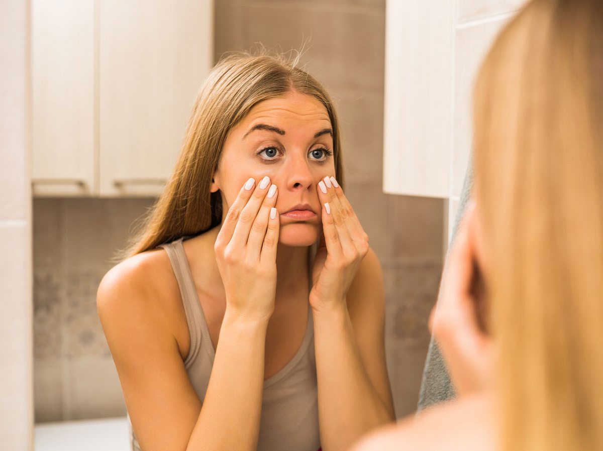Frau betrachtet ihre Augen im Spiegel, ob sie Tränensäcke hat