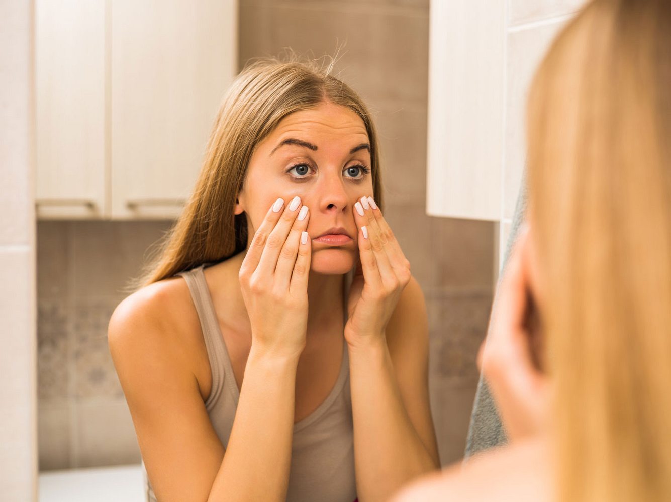 Frau betrachtet ihre Augen im Spiegel, ob sie Tränensäcke hat