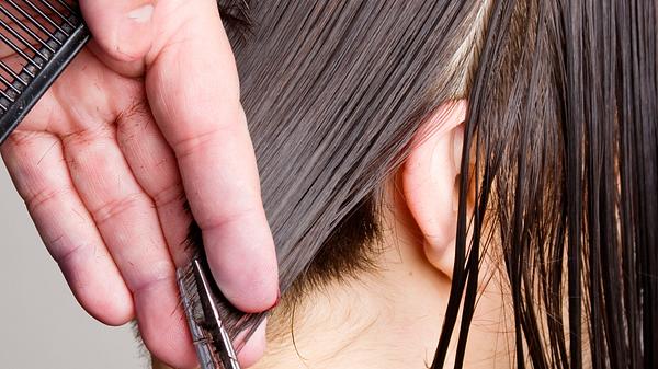 Jemand schneidet braune Haare im Nacken mit einer Schere. - Foto: numbeos/iStock (Themenbild)