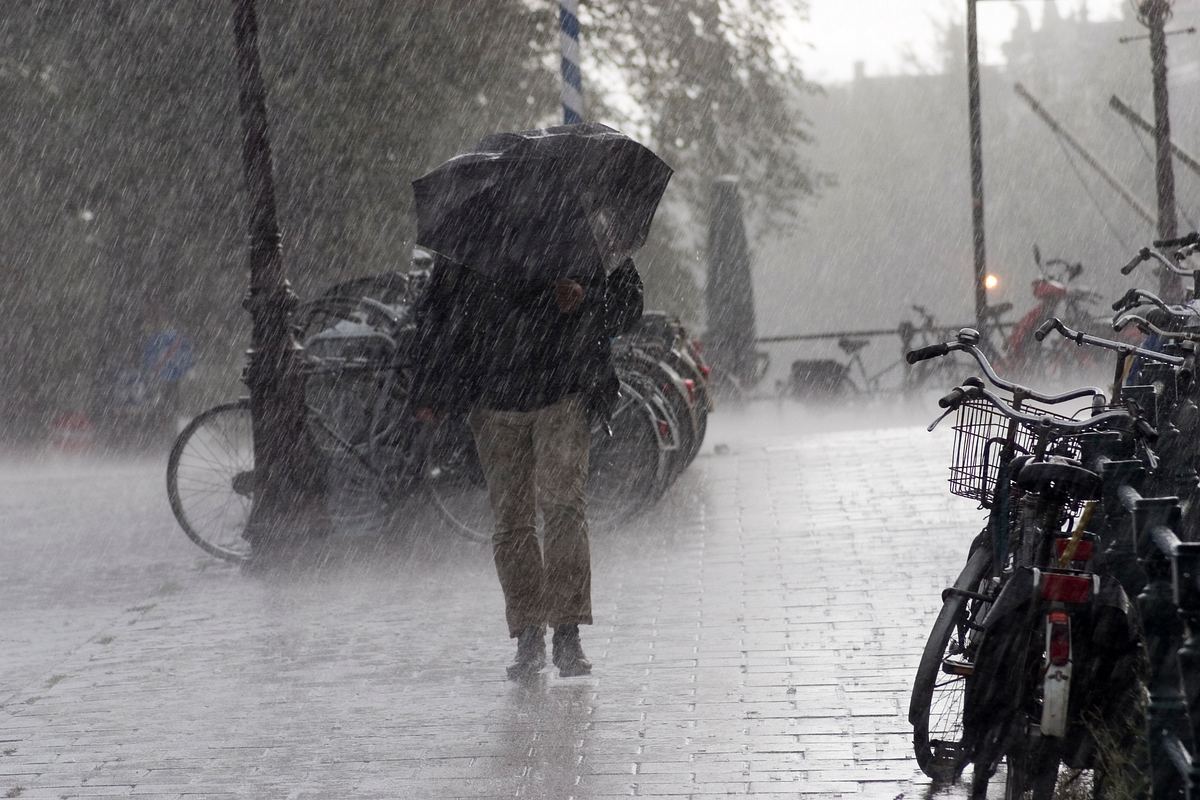 Frau, die in einer Fußgängerzone einen schwarzen Regenschirm hält, um sich vor starkem Wind und Regen zu schützen.