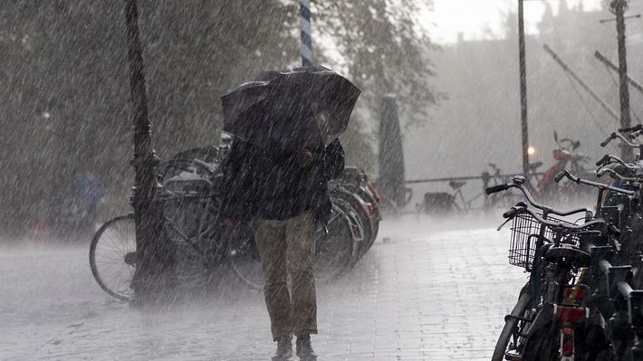 Frau, die in einer Fußgängerzone einen schwarzen Regenschirm hält, um sich vor starkem Wind und Regen zu schützen. - Foto: Doctor_bass/iStock