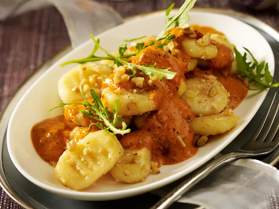Selbstgemachte Gnocchi mit Soße und Rucola auf einem ovalen Teller.