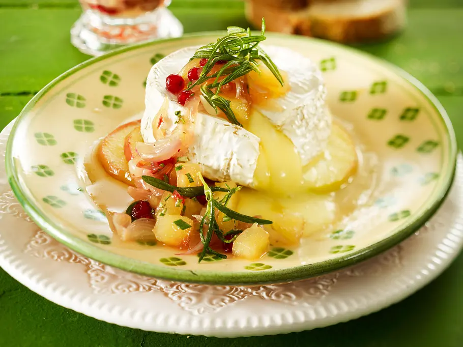 Aufgeschnittener gebackener Camembert mit Apfel-Chutney und Rosmarin als Dekoration.