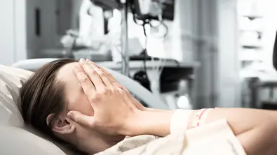 Frau liegt im Kreißsaal und verdeckt ihr Gesicht mit den Händen. - Foto: kieferpix / iStock