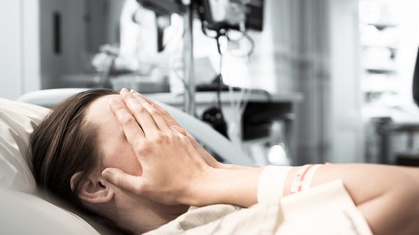 Frau liegt im Kreißsaal und verdeckt ihr Gesicht mit den Händen. - Foto: kieferpix / iStock