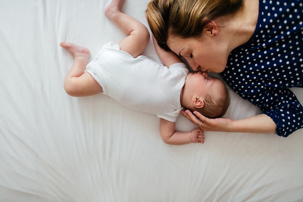 Frau liegt mit einem Baby auf dem Bett und küsst es auf die Nase (Themenbild)