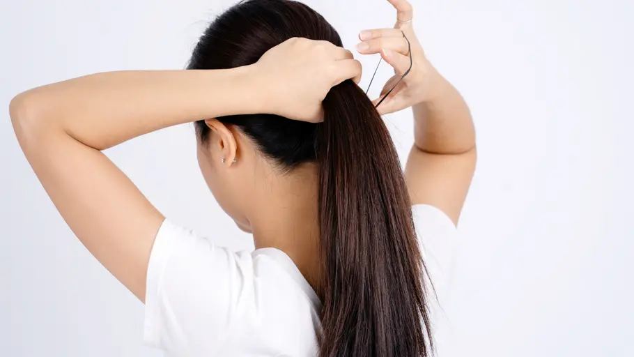 Frau mit langen, dunklen Haaren, macht sich einen Pferdeschwanz Frau mit langen, dunklen Haaren, macht sich einen Pferdeschwanz