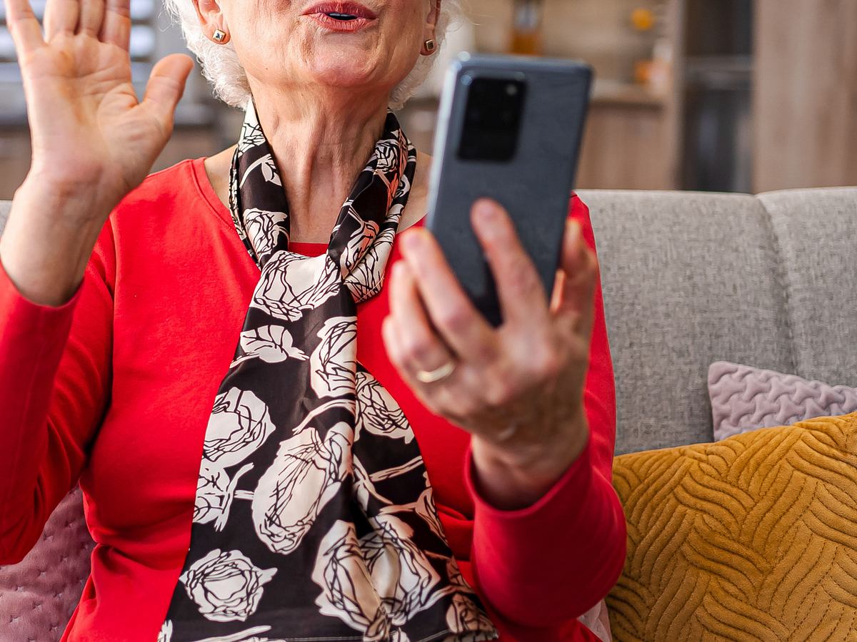 Unerkennbare pensionierte Seniorin nimmt mit ihrem Smartphone im Wohnzimmer ein Video auf.