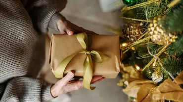 Jemand hält ein Geschenkt an den Weihnachtsbaum. - Foto: iStock/OksanaKlymenko