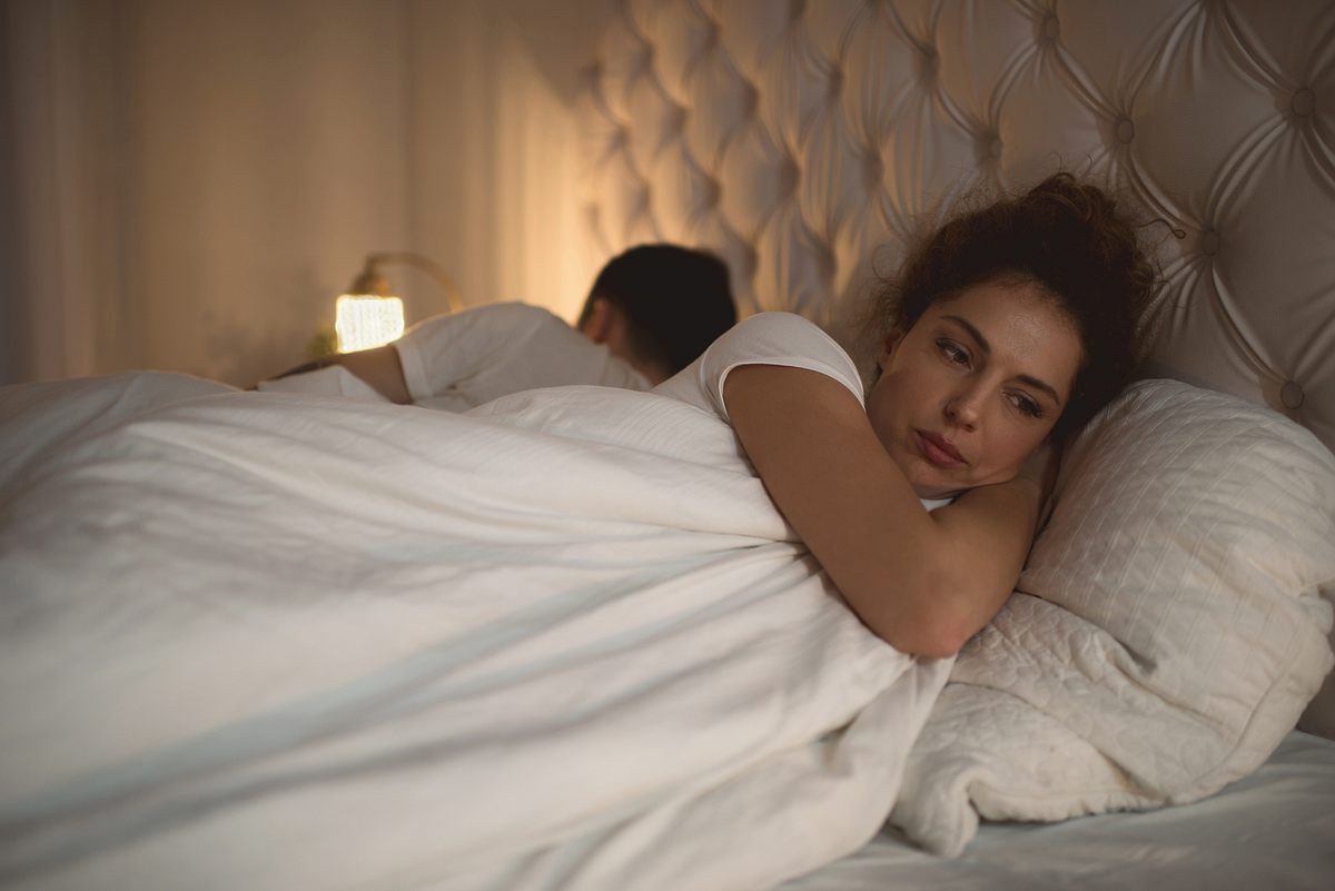 Frau liegt neben Partner im Bett und ist nachdenklich.